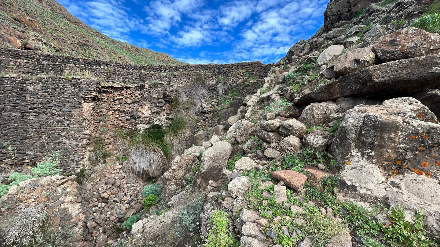 Wanderweg durch grobe Gesteinsblöcke rechts der Staumauer