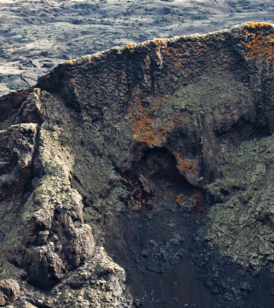 flechtenbewachsene Abbruchkante des Montaña del las Lapas o del Cuervo in umliegender Mondlandschaft