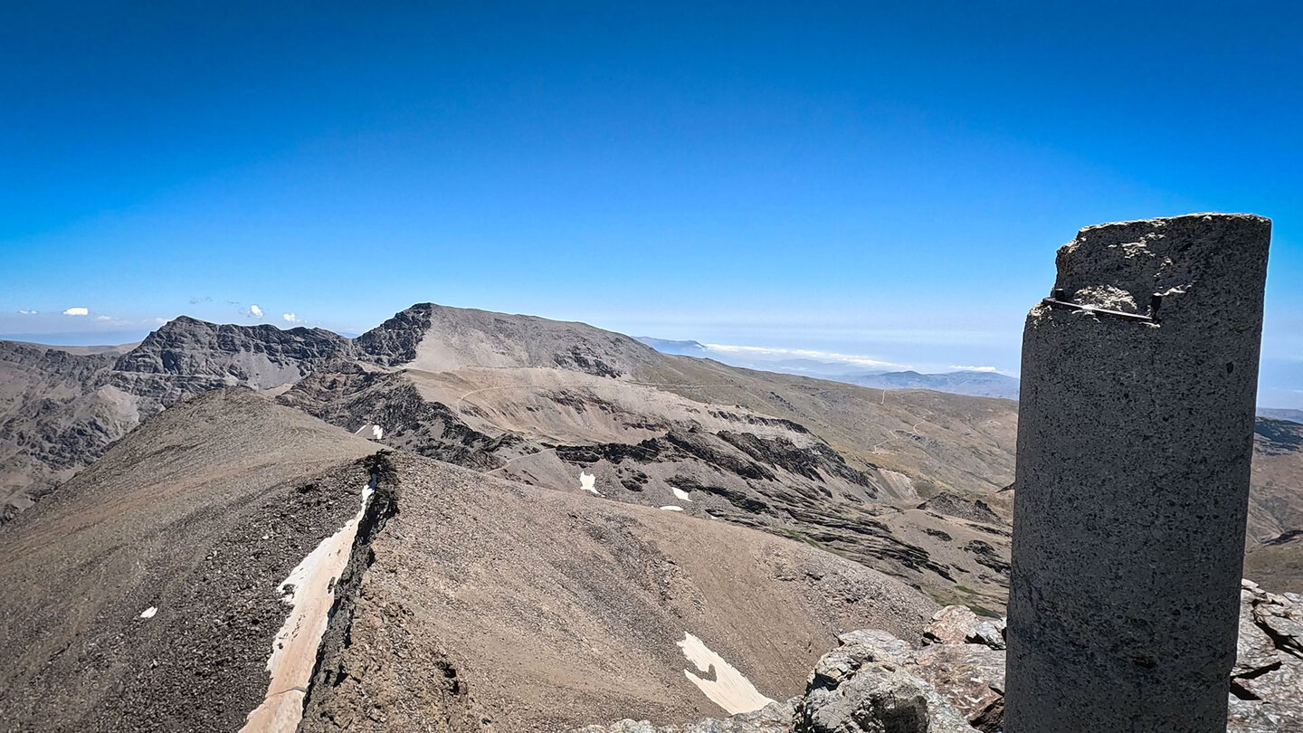 Gipfelsäule auf dem Pico del Veleta mit Blick auf den Mulhacén im Nationalpark Sierra Nevada